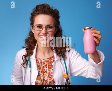 Sorridente pediatra donna in bianco manto medico una bottiglia di bere yogurt isolato su blu Foto Stock