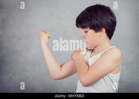 Kid che mostra i suoi muscoli su sfondo grigio Foto Stock