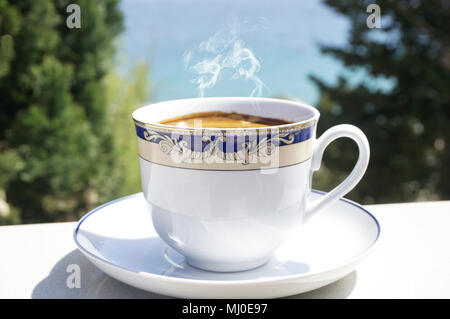 Tazza di caffè caldo sulla terrazza a mare sfocata e alberi in background Foto Stock