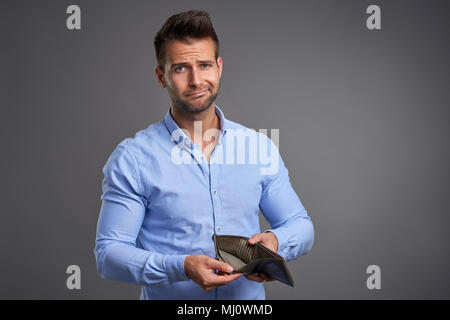 Un povero bel giovane sensazione ha sottolineato guardando la telecamera e mostrando il suo portafoglio vuoto. Foto Stock