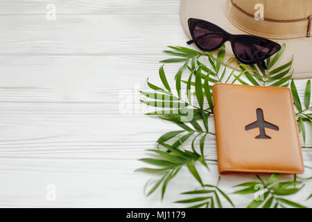 Passaporto con piano e hat nero con occhiali da sole retrò sul verde foglie di palmo in bianco sullo sfondo di legno. spazio per il testo. moderna viaggi e vacanze im Foto Stock