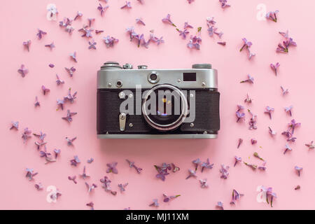 Elegante vecchia foto fotocamera su sfondo rosa con fiori lilla. viaggio creativo alla moda laici piatta con spazio per il testo. moderna moda e hipster immagine. Foto Stock