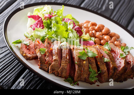 A fette grigliate di carne asada bistecca con lattuga e fagioli close-up su una piastra orizzontale. Foto Stock