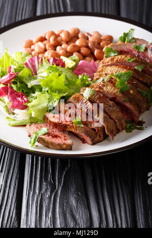 Grigliate di carne di manzo con insalata verde e fagioli close-up su una piastra sul piano verticale. Foto Stock