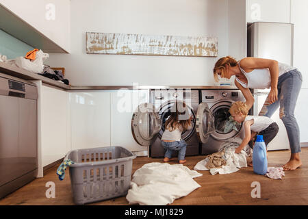 Madre e bambini nella stanza lavanderia con lavatrice o asciugatrice.  Incombenze familiari. Moderni dispositivi domestici e di detersivo di  lavaggio in bianco sunny hom Foto stock - Alamy