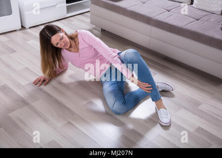 Donna cadere sul pavimento di legno che soffrono di dolore alle gambe Foto Stock