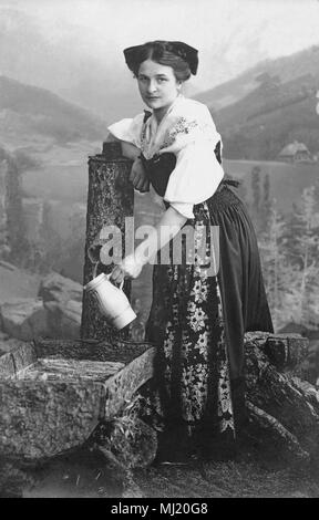 Donna in costume tradizionale del riempimento di una brocca con acqua al pozzo, 1910s, Germania Foto Stock