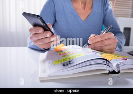 Close-up di una donna utilizzando il telefono cellulare con il diario sulla scrivania Foto Stock