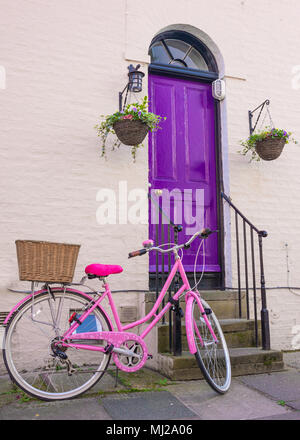 Rosa luminoso donna bicicletta posteriore con cesto in vimini parcheggiata di fronte una viola in legno porta anteriore di un vittoriano classico stile britannico house Foto Stock