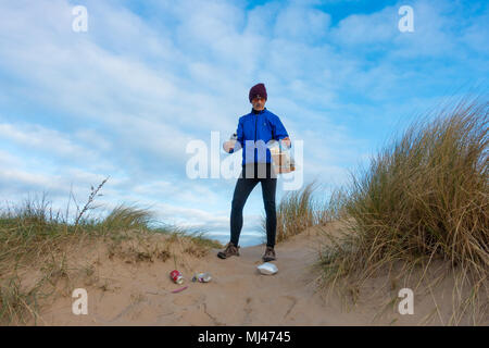 Un pareggiatore Plogging (prelievo di lettiera durante il jogging) sulla sua corsa mattutina attraverso le dune di sabbia.UK Foto Stock