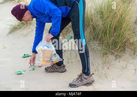 Un pareggiatore Plogging (prelievo di lettiera durante il jogging) sulla sua corsa mattutina attraverso le dune di sabbia.UK Foto Stock