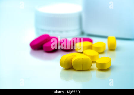 Pila di giallo e rosa compresse pillole su sfondo sfocato di pillole di plastica bottiglia con copia spazio. Ibuprofene per il sollievo del dolore. Industr farmaceutica Foto Stock