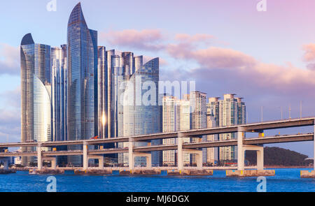 Busan, Corea del Sud. Paesaggio urbano del quartiere di Haeundae con grattacieli di lusso e ponte nella luce della sera Foto Stock