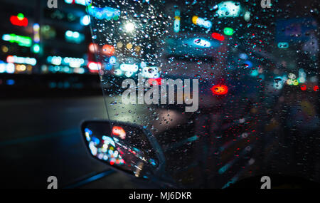 Abstract città notte sfondo sfocato, riflessi colorati e gocce di pioggia sul bagnato parabrezza scooter Foto Stock