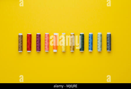 Colorate rocchetti di filo in una fila più luminoso dello sfondo giallo, sopra visualizza Foto Stock