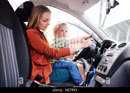 Madre con un bambino piccolo si siede dietro al volante di un'auto. Viaggio di famiglia Foto Stock