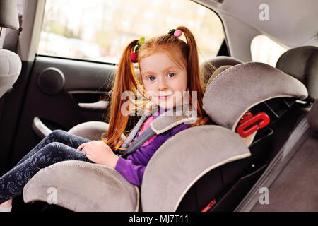 Baby poco i Capelli rossi ragazza sorridente mentre è seduto in un seggiolino per auto per bambino. Foto Stock