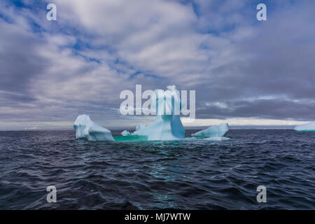 Una forma inusuale blu brillante iceberg galleggianti in mare contro un blu e il cielo nuvoloso, Antartide Foto Stock