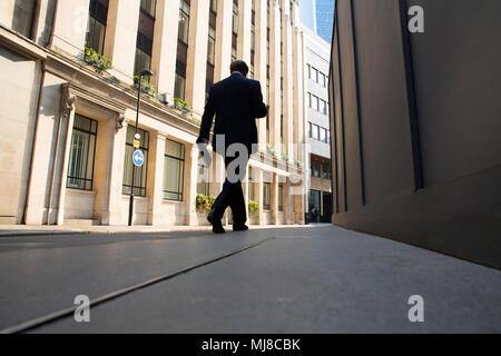 Basso angolo vista posteriore dell'uomo vestito da indossare a piedi lungo la strada urbana. Foto Stock
