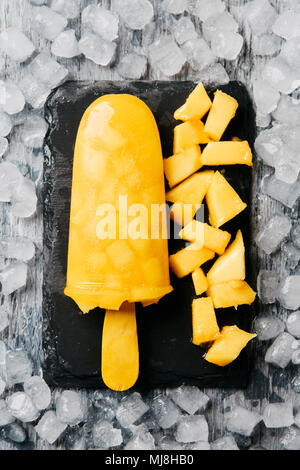 Elevato angolo di vista a casa ice pop, fatta con succo naturale di frutta e pezzi di frutta, posto su un vassoio di ardesia, sul ghiaccio tritato Foto Stock
