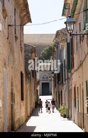 Alcudia, Mallorca, Spagna. 2018. La famiglia in cammino verso la chiesa parrocchiale lungo una strada stretta nell'area della città vecchia di Alcudia. Foto Stock