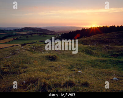 Visualizza SW al tramonto dalla cima della collina di Gop cairn, verso Moel Hiraddug hillfort, con montagne di Snowdonia in distanza. Trelawnyd, N Galles Foto Stock