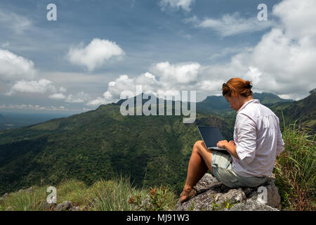 Ragazza caucasica lavorando sul suo computer sulla cima della montagna. Concetto di lavoro remoti o in internet per frilancer Foto Stock