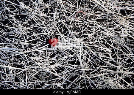 Un rosso cuore di vetro al centro di un groviglio di i ritagli di carta su uno sfondo di ardesia. Foto Stock