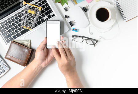 Uomo di business utilizzando il telefono cellulare per lo shopping online su bianco scrivania da ufficio tavolo con altri materiali e la tazza di caffè sul fondo bianco con vista superiore Foto Stock