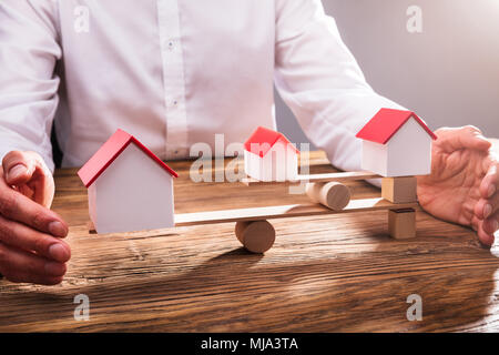 Close-up di commercianti la mano che copre l'equilibrio tra il modello di casa su altalena in Office Foto Stock