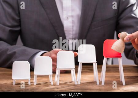 Close-up di commercianti del dito immissione pedina sulla sedia rossa sulla scrivania in legno Foto Stock