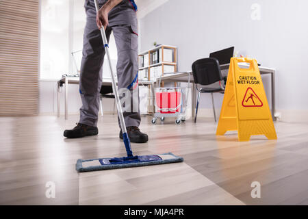 Sezione bassa di bidello maschio piano di pulizia con segnale di avvertimento pavimento bagnato in Office Foto Stock