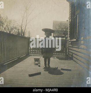 Antique c1902 fotografia, toddler boy in capi di abbigliamento in stile vittoriano con tirare giocattolo e blocchi sul portico. Posizione sconosciuta, probabilmente la Nuova Inghilterra, Stati Uniti d'America. Fonte: originale stampa fotografica. Foto Stock