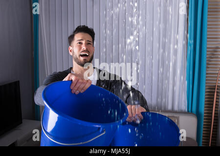 Close-up di un giovane uomo con la benna e la raccolta di acqua dal soffitto Foto Stock