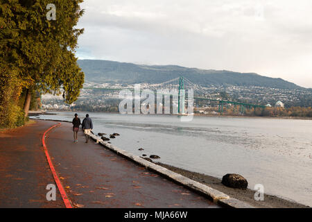 Giovane camminando sulla Stanley Park Seawall durante la stagione autunnale. Il Golden Bridge e North Vancouver in background. Foto Stock