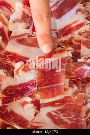 Vista superiore del prosciutto Serrano piastra e donna puntare il dito per affettare, concentrarsi sulla fetta Foto Stock