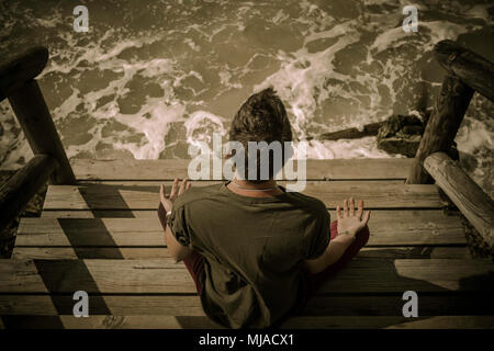 Meditando sulle scale di legno di fronte al mare Foto Stock