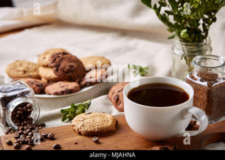 La colazione ancora in vita con tazza di caffè sul tagliere, ribaltato il vaso con i chicchi di caffè, biscotti dolci sulla tovaglia homespun, il fuoco selettivo clos Foto Stock