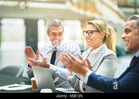 Coppia gruppo di imprenditori seduti insieme ad un tavolo in un ufficio battendo le mani durante una presentazione Foto Stock