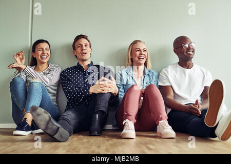 Gruppo di diversi imprenditori ridere insieme mentre è seduto sul pavimento di un ufficio durante la loro sosta Foto Stock