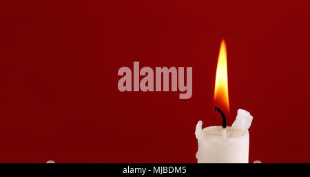 La parte superiore di un bianco candela che brucia con una fiamma su sfondo rosso con emty spazio. Foto Stock
