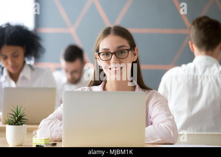 Donna sorridente guardando la telecamera seduto alla scrivania in collaborazione Foto Stock