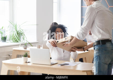 Sorridente dipendente africano tenendo la pizza dal corriere, ufficio cibo Foto Stock