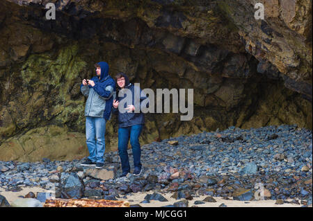 Fratelli trovare un riparo dal vento e dalla pioggia in un scolpito nella sezione di un grande hillsdie sulla costa dell'Oregon. Uno è di prendere il cellulare mentre le foto Foto Stock