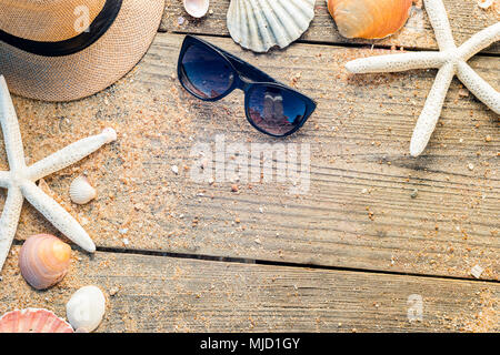 Estate accessori come hat, conchiglie e occhiali da sole in legno e lo sfondo di sabbia Foto Stock
