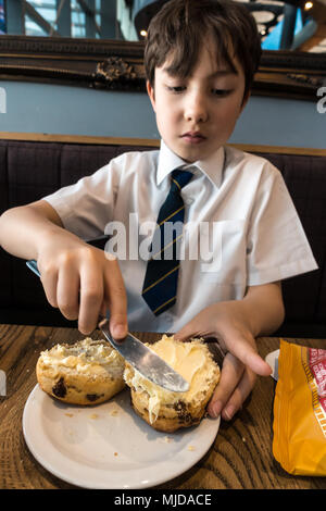 Un giovane ragazzo godendo di un frutto scone e rabboccato con clotted cream e confettura di lamponi. Foto Stock