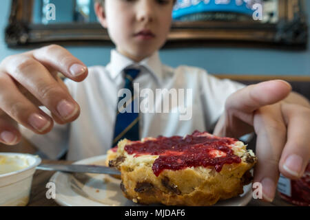 Un giovane ragazzo godendo di un frutto scone e rabboccato con clotted cream e confettura di lamponi. Foto Stock