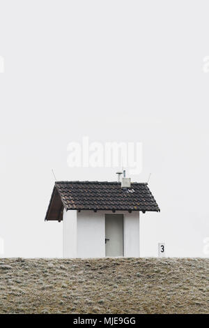 Piccola casa su una diga in inverno, cielo grigio bianco, brina Foto Stock