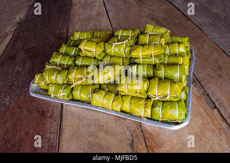 Banane con il riso appiccicoso avvolto con foglie di colore marrone su sfondo di legno. Khao Tom Mat. Foto Stock