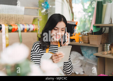 Femmina asiatica fioraio chiamando sullo smartphone e di rendere note al negozio di fiori counter Foto Stock